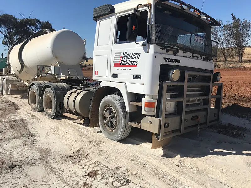 A Volvo cement tanker truck with "Western Stabilisers" logo, parked on a dusty road in a rural area.