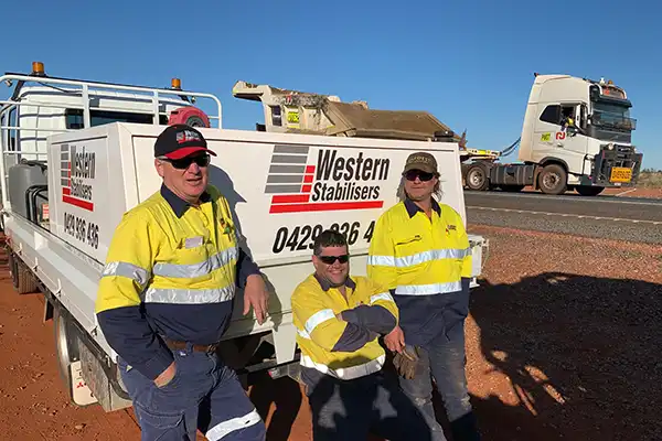 Three workers in high-visibility clothing lean against a truck labeled "Western Stabilisers," specializing in soil stabilisation, with a semi-truck in the background.