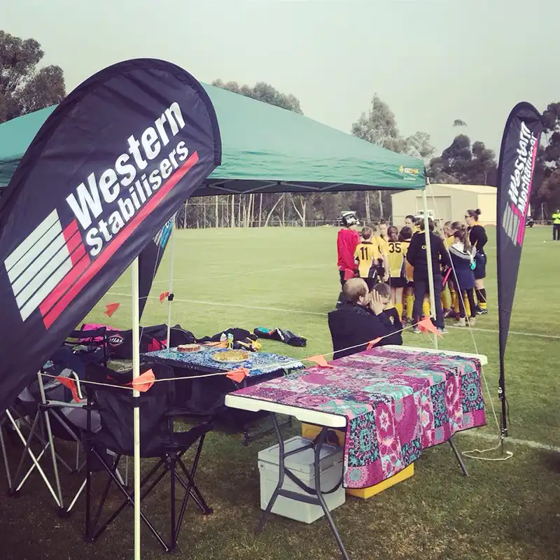 Outdoor event setup with branded tents and banners, colorful tablecloths on tables, and a group of people huddling in the background.