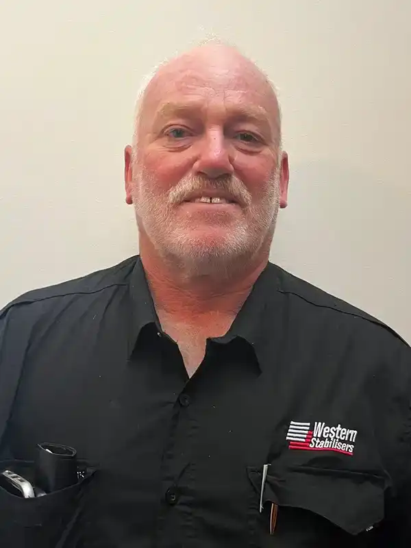 A man with a white beard wearing a black "Western Stabilisers" shirt stands against a plain background.